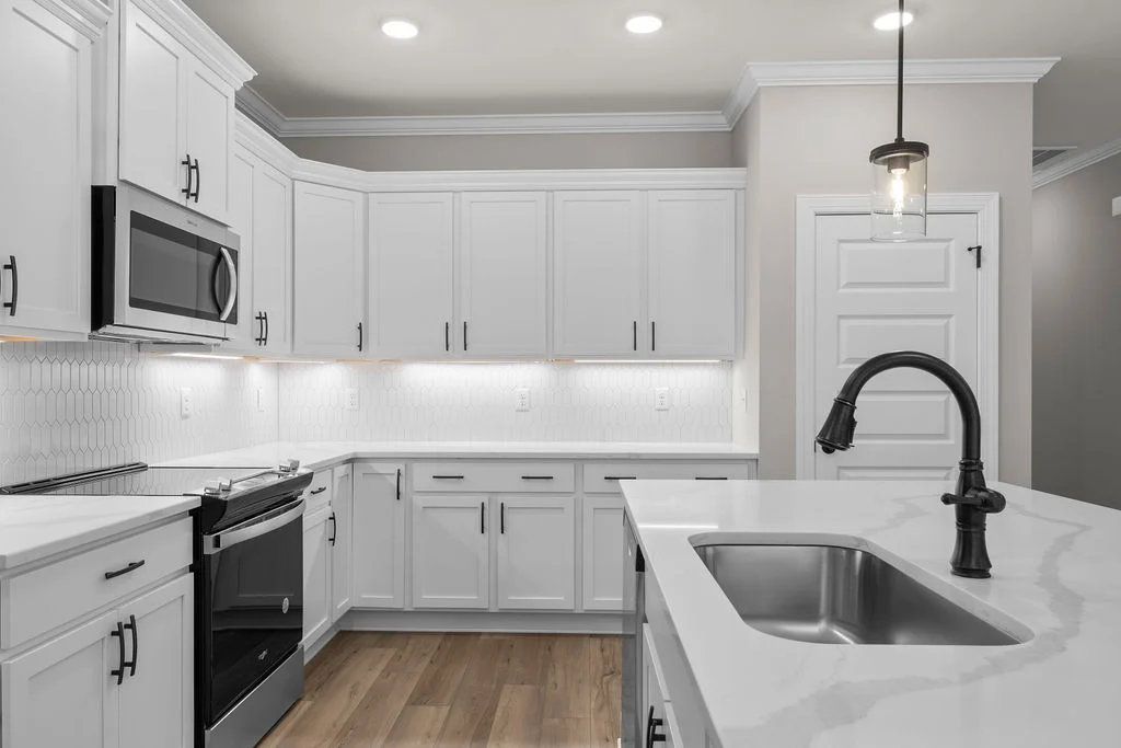Modern kitchen with white cabinets, black appliances, and sleek faucet under pendant lighting. Designed by Pratt Home Builders in Chattanooga TN.