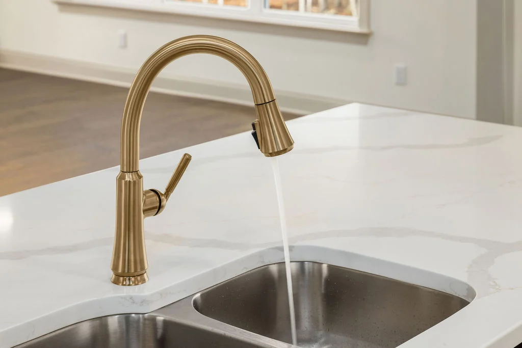 Bronze kitchen faucet with running water over a double sink, designed by Pratt Home Builders in Chattanooga TN.