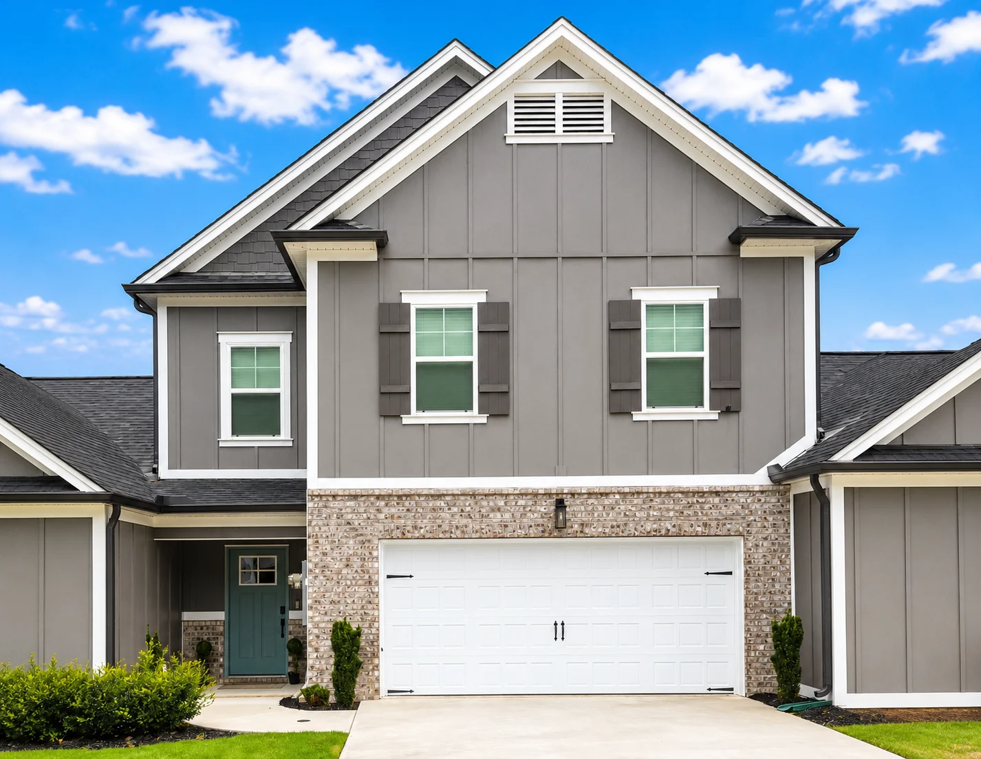 Modern gray and brick home with white garage and blue door, under bright sky. Built by Pratt Home Builders in Chattanooga TN.