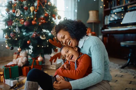 Mother and child laughing by a decorated Christmas tree, surrounded by gifts, embodying warmth similar to Pratt Home Builders in Chattanooga TN.